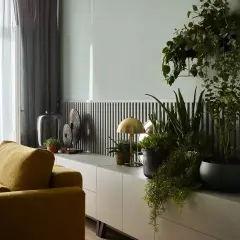 Miękkie, żółte fotele obok komody z roślinami. W tle zasłony w odcieniu **kolor szary** i ściana w pionowe pasy.