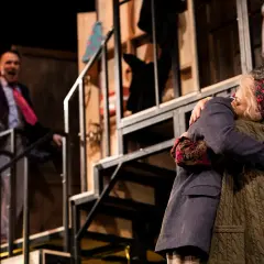 Na scenie Teatru Osterwy wzruszające objęcie dwóch postaci. W tle mężczyzna w garniturze krzyczy, co nie widać.