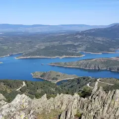 Vista panorámica del embalse de Puentes Viejas, con sus aguas azules serpenteando entre colinas verdes y montañas al fondo.
