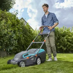 Mężczyzna z kosiarką elektryczną, która jest jedną z najlepszych kosiarek elektrycznych, dba o swój zielony trawnik.