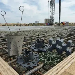 Na budowie widać zbrojenie i świeży beton. Na pierwszym planie leżą podkładki pod zbrojenie, które zapewnią odpowiednią grubość otuliny betonowej.