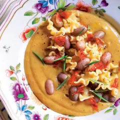 Pasta e Fagioli with ruffled pasta, beans, and crispy pancetta on a floral plate.