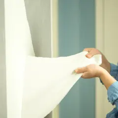 Dłonie zdejmujące białą tapetę ze ściany.