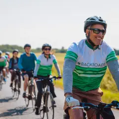 A group enjoys family cycling holidays on a sunny day, riding bikes down a paved path through golden fields.