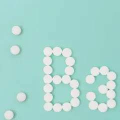 Białe tabletki ułożone w kształt litery "B" i cyfry "3" na turkusowym tle. To symbol witaminy B3.