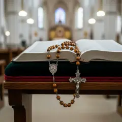 Otwarta księga i drewniany różaniec część radosna na ławce w kościele.