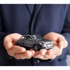Mani che sorreggono un modellino d'auto grigio. Non dimenticare la tua assicurazione scaduta 15 giorni fa!