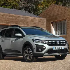 Dacia Jogger grigio metallizzato, un'auto che consuma meno GPL, parcheggiata davanti a una casa moderna in legno.