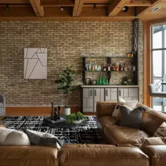 A rustic modern living room with exposed brick, wood beams, a leather sofa, and a home bar.