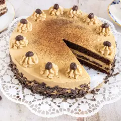 Eine köstliche Mokka Torte, verziert mit Kaffeebohnen und Schokostückchen, wartet auf Genießer. Daneben ein Stück Torte und eine Tasse Kaffee.