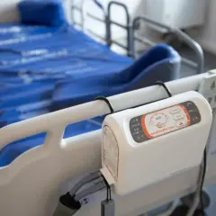 Łóżko szpitalne z niebieskim materacem przeciwodleżynowym i panelem sterowania.