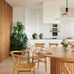 Comedor y cocina modernos con pared de lamas de madera, planta grande, mesa redonda y dos lámparas de techo.