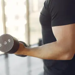 Mężczyzna wykonuje ćwiczenia na biceps z hantlem 10 kg. To jedne z najlepszych ćwiczeń na biceps.