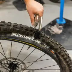 Ręka z kombinerkami zaciska oponę rowerową, która jest zwijana, a nie drutowa.