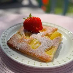 En bit saftig ananaskaka i långpanna, pudrad med florsocker och toppad med en färsk jordgubbe. Perfekt för en sommardag.