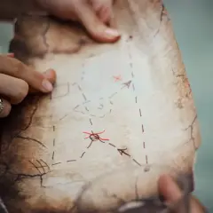 Dwie dłonie trzymają starą mapę z zaznaczonymi trasami i krzyżykami.