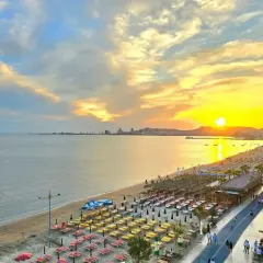 Zachód słońca nad Durrës plaża. Rzędy leżaków i parasoli czekają na plażowiczów, a w oddali widać panoramę miasta.