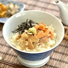 A delicious ochazuke recipe featuring rice, flaked salmon, nori, and wasabi in a blue-striped bowl, with a teapot in the background.