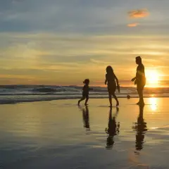 Rodzina cieszy się zachodem słońca na plaży. Dzieci biegną po mokrym piasku, a rodzic obserwuje. To była duża zabawa biegowa.