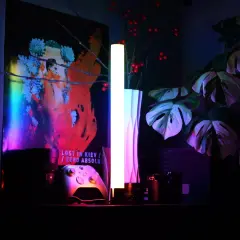 Na półce stoją kontroler do gier, aparat i lampa, której światło RGB tworzy nastrojową atmosferę.