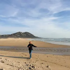 Mujer corre en la playa de Muros, Galicia, con montañas al fondo y el mar azul.