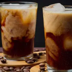 Två glas med krämigt iskaffe, perfekt för ett enkelt iskaffe recept. Kaffebönor sprider sig runt glasen.