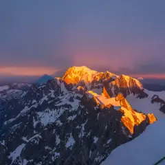 Złote światło wschodu słońca oświetla szczyt Mont Blanc, rzucając długi cień na ośnieżone góry.