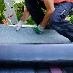 Handwerker klebt Dachpappe. Mit Handschuhen wird die Bitumenbahn sorgfältig ausgerollt und befestigt, um das Dach wetterfest zu machen.