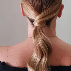 Capelli biondi raccolti in una coda bassa con un'elegante torsione, perfetta per una cerimonia.