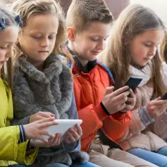 Dzieci skupione na ekranach telefonów i tabletu, szukają najlepszych gier dla 4 latka na telefon.