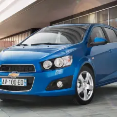 Błękitny Chevrolet Aveo stoi przed nowoczesnym budynkiem.