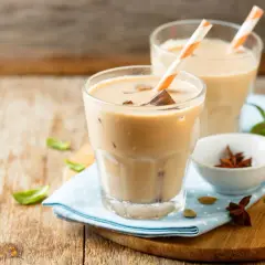Dwa orzeźwiające **chai latte** z kostkami lodu i słomkami, ozdobione listkami mięty i przyprawami.