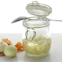 Słoik z domowym syropem z cebuli, obok dwie cebule i łuski. Łyżeczka oparta o słoik.