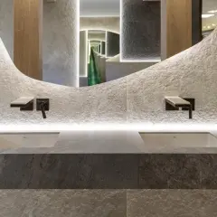 Nowoczesna łazienka z dwoma umywalkami, kamiennymi płytkami i rośliną, idealnie oddająca zasady biophilic design.