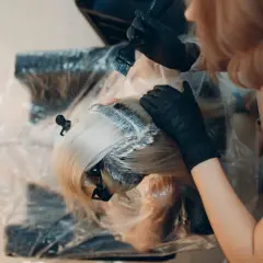 Fryzjerka nakłada farbę na blond włosy. Czas, ile trzymać farbę na włosach, zależy od efektu, jaki chcemy uzyskać.