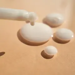 Ein weißes Serum tropft aus einem Applikator auf eine beige Oberfläche. Das ist Panthenol, ein Wirkstoff für Haut und Haar.