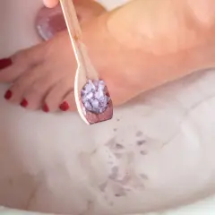 Un cucchiaio di sali per pediluvio fai da te viene versato in una vasca, pronto per un bagno rilassante per i piedi.