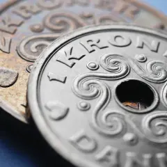 Dwie monety, jedna srebrna z napisem "1 KRONE DANMARK" i otworem pośrodku, druga miedziana z sercem. DKK jaka to waluta?