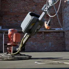 Zacieraczka do posadzek pracuje na budowie, wygładzając świeży beton. Robotnik w niebieskich spodniach nadzoruje pracę maszyny.