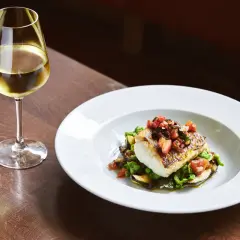Piatto di pesce con verdure e un bicchiere di ribolla gialla.