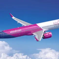 Samolot Wizz Air lecący na tle błękitnego nieba z chmurami.