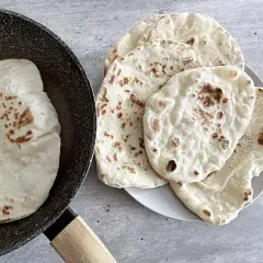 Chlebek naan przepis: świeżo usmażone placki na patelni i talerzu, gotowe do podania.