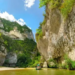 Wąwóz Gorges du Tarn, zielona rzeka i łódź z wioślarzami wśród skalnych ścian porośniętych bujną roślinnością.