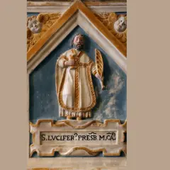 Rzeźba św. Lucifera, prezbitera, w białej szacie z palmą męczeństwa i kielichem. Nad nim dwa aniołki.