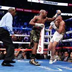 A referee watches as Floyd Mayweather Jr. lands a punch on Conor McGregor during their boxing match.