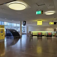Dwa żółte automaty biletowe Arlanda Express, obok schodów ruchomych. Sprawdź arlanda express cena przed podróżą.