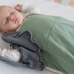 A baby sleeps soundly in a green sleep sack, a grey elephant toy peeking out. This image inspires thoughts on how to make baby clothes.