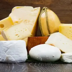 Varietà di formaggi, tra cui spicca un formaggio pasta filata dalla forma tondeggiante, su un tavolo di legno scuro.