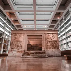 L'Ara Pacis, un altare monumentale con rilievi antichi, si erge maestoso in un moderno spazio espositivo con ampie vetrate.