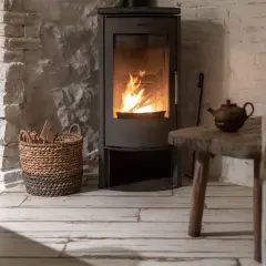 Un poêle à bois moderne diffuse une chaleur réconfortante, parfait pour un chauffage central cosy. Une théière ancienne et un panier de bois complètent l'ambiance rustique.